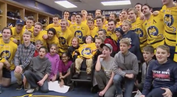 Michael Torello is smiling wide with the Quinnipiac men's hockey team behind him as they pose for a photo in the locker room